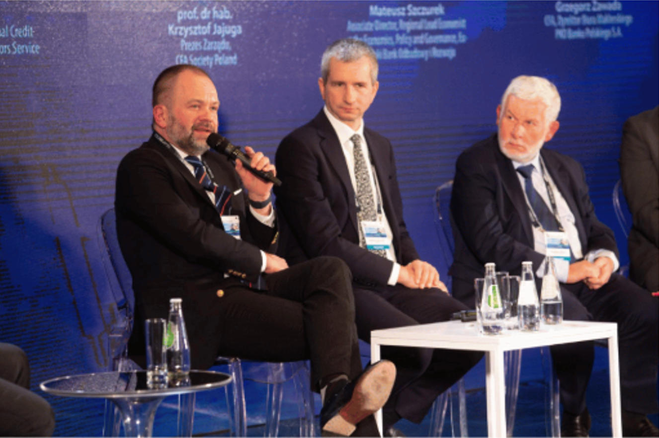 [Zdjęcie: Panel XXIV Konferencji Rynku Kapitałowego. Od lewej: z mikrofonem w dłoni Grzegorz Zawada, Mateusz Szczurek oraz prof. dr hab. Krzysztof Jajoga.]
